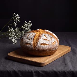 Sourdough boule on a wooden board over dark linen — artisan bread product photography