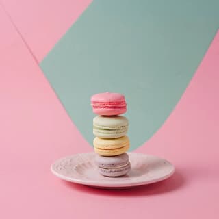Pastel French macaron stack on pink with a sage-mint color block — brand-color food photography