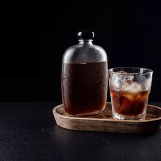 Cold brew coffee flask and iced glass on a black surface — drink product food photography