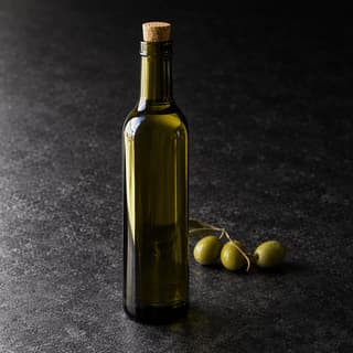 Single unlabelled dark green glass bottle of extra virgin olive oil with a cork stopper, lit by one narrow highlight running down its shoulder