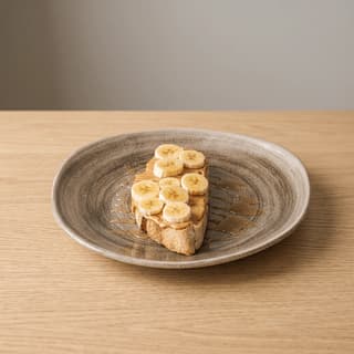 Tosta com manteiga de frutos secos e banana num prato de grés — fotografia de alimentos com sugestão de apresentação