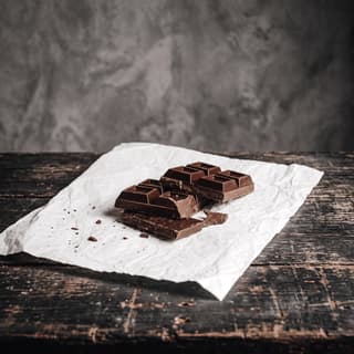 Snapped dark chocolate bar on parchment over weathered dark wood — bean-to-bar chocolate photography