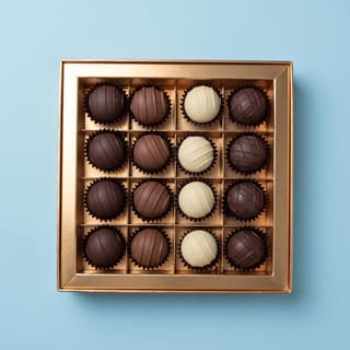 Open gold gift box of sixteen truffles on pastel blue — chocolate gift photography