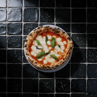 Whole margherita pizza on black tiles from overhead — pizza campaign food photography
