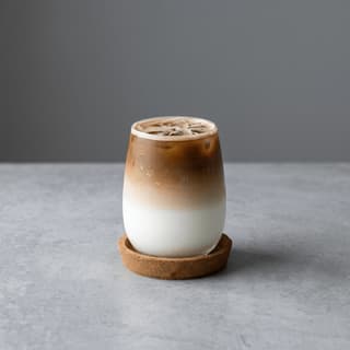 Layered iced latte on a cork coaster and gray concrete — café iced coffee photography
