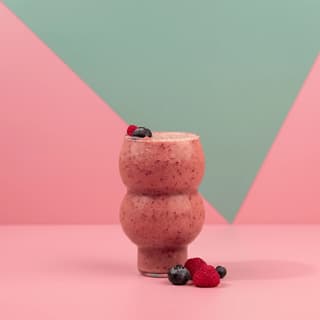 Mixed berry smoothie in a bubble glass on pastel pink — juice bar photography
