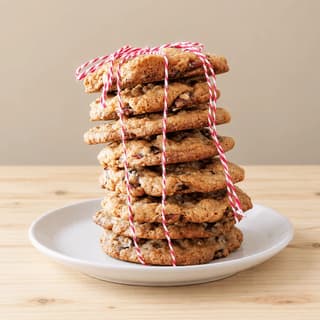 Tall stack of eight oatmeal cookies with cranberries and pecans tied with red-and-white baker's twine on a white plate over pale pine