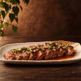 Nakrájený opečený ribeye rozložený do vějíře na krémovém kropenatém talíři s hrubým zeleným chimichurri a výpekem