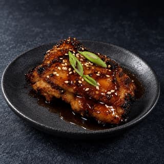 Single sticky honey soy glazed grilled chicken thigh with a high lacquered shine on a dark slate plate