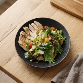 Grilled chicken quinoa bowl with greens on blonde oak — fast-casual brand food photography