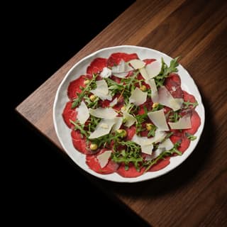 Beef carpaccio with arugula and parmesan on a white plate — restaurant starter food photography