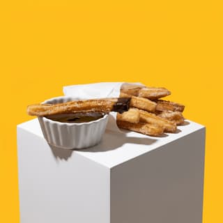 Sugar-coated churros with chocolate sauce on a white cube — dessert truck flyer photography