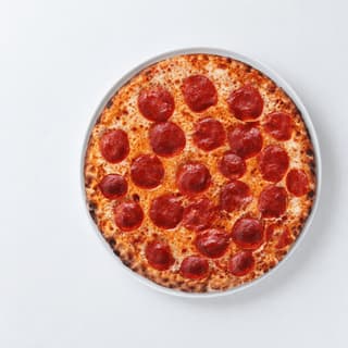 Whole thin-crust pepperoni pizza with glossy pepperoni rounds and golden melted mozzarella on a white plate, shot from directly overhead