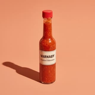 Smoked habanero hot sauce bottle on a coral color sweep — sauce brand product photography