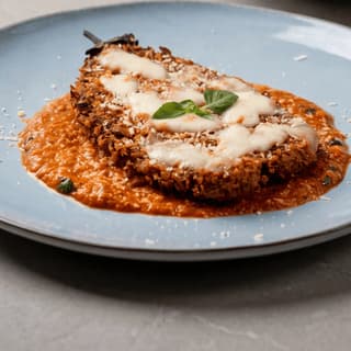 Eggplant parmesan with melted mozzarella on a blue plate — grand opening flyer food photography