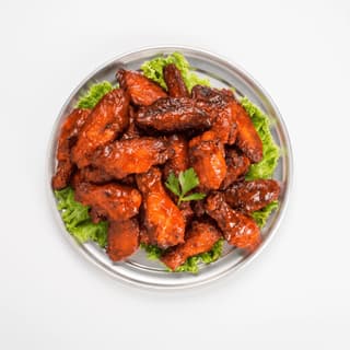 Glazed chicken wings on lettuce on a silver plate — delivery flyer food photography