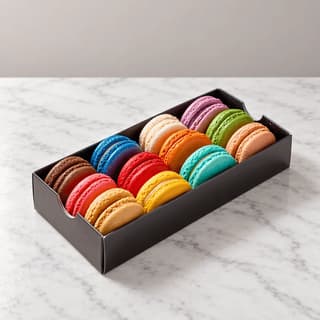 Open white gift box of twelve pastel macarons in four colours on white marble with the lid resting beside it