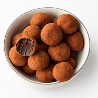 Small pile of cocoa-dusted dark chocolate truffles on a plain white plate against a seamless white background, each sphere keeping its shape