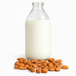 Tall unlabelled clear glass bottle of creamy white almond milk with a few whole almonds, white-on-white against a seamless pure white background