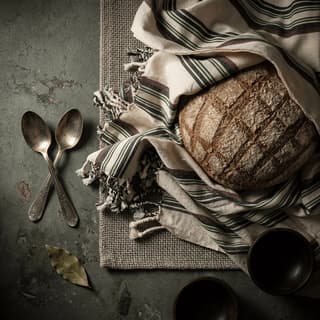 Rustic sourdough boule with blistered mahogany crust and scored ear on dark walnut board — artisan bread photography