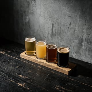 Wooden tasting paddle holding four small glasses of beer running from pale straw to opaque black