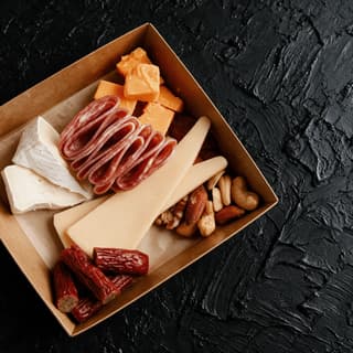 Open shippable charcuterie gift box with compartments of cured meat, cheese, nuts and jam