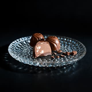 Single dark chocolate bonbon cut clean in half standing upright showing a smooth caramel ganache layer under a thin glossy shell