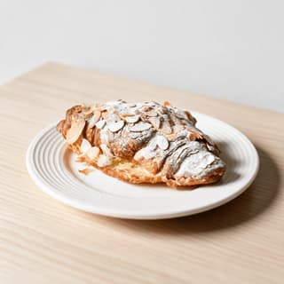 Flaked almond croissant dusted with icing sugar on a small ceramic plate