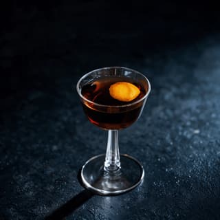 Single amber cocktail in a coupe glass with an expressed citrus twist on a dark slate surface