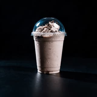 Thick chocolate milkshake in a clear cup with whipped cream against a deep blue studio backdrop