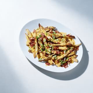 Loaded fries topped with melted cheese sauce and bacon pieces in a paper tray on a white surface