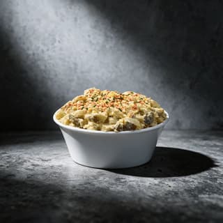 Phần salad khoai tây béo mịn rắc ớt bột paprika và hẹ cắt nhỏ trong hộp deli trắng trơn