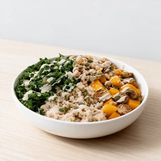 One build-your-own grain bowl with chickpeas, roasted squash, greens and tahini drizzle in a wide shallow bowl