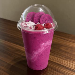 Clear to go cup of bright pink dragon fruit smoothie with a domed lid on a dark walnut counter