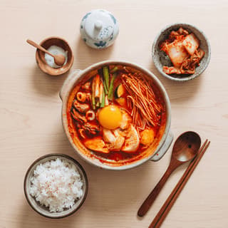 Soondubu jjigae silken tofu stew bubbling stone pot red broth egg scallion overhead — soondubu hero photography