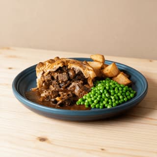 London gastropub steak and ale pie burnished puff pastry cut open braised beef mushrooms dark ale gravy roast potatoes peas — steak pie hero photography