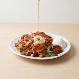 Iskender kebab doner over pide bread tomato sauce yogurt butter pour plate — iskender hero photography