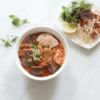 Bun bo hue spicy sour beef noodle soup lemongrass chili oil pork shank herbs bowl — bun bo hue hero photography