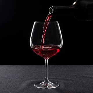 Burgundy Pinot Noir mid-pour into hand-blown crystal Burgundy glass with backlit ruby translucency — French wine photography