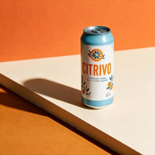 Yerba mate can on cream plinth against orange color-block backdrop with hard shadow — editorial beverage photography