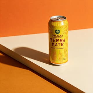 Yerba mate can on cream plinth against orange color-block backdrop with hard shadow — editorial beverage photography