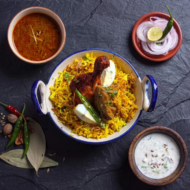 Hyderabadi biryani handi saffron basmati raita boiled egg overhead slate — biryani card photography