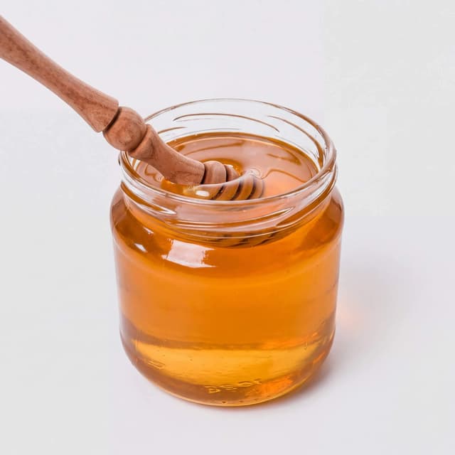 Unlabelled glass jar of golden honey with wooden dipper on white — Amazon listing food photography