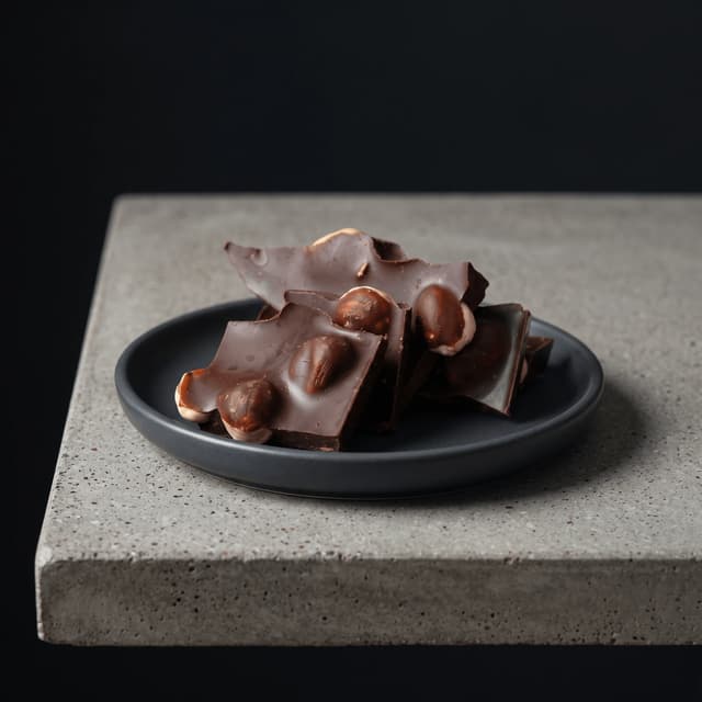 Snapped hazelnut dark chocolate on a charcoal plate and concrete — bean-to-bar photography