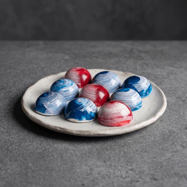 Hand-painted blue and red bonbons on a stoneware plate — chocolatier product photography