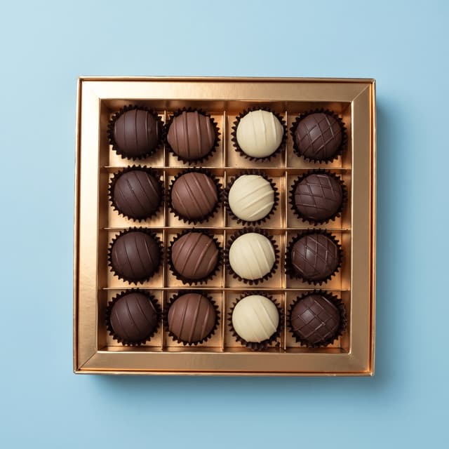 Open gold gift box of sixteen truffles on pastel blue — chocolate gift photography