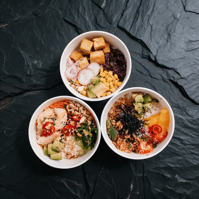 Three poke bowls on dark slate from overhead — bowl menu campaign food photography