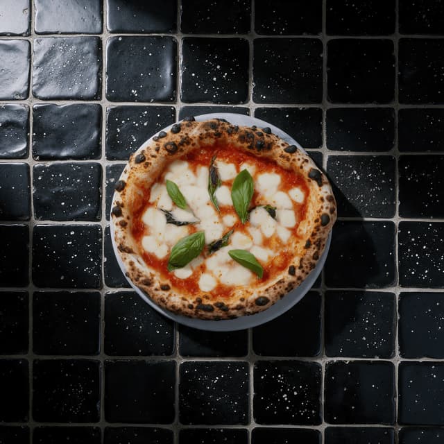 Whole margherita pizza on black tiles from overhead — pizza campaign food photography