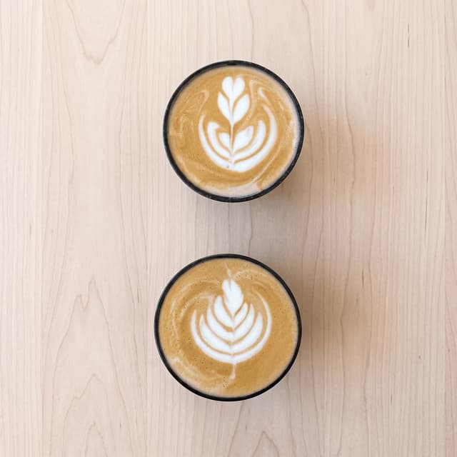 Two lattes with latte art on pale wood, seen from above — café coffee photography