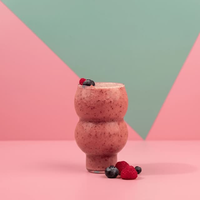 Mixed berry smoothie in a bubble glass on pastel pink — juice bar photography